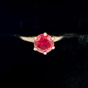 May include: A close-up of a ring with a red gemstone set in a silver band.