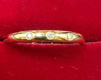 May include: A thin gold band with three small diamonds set in the band.