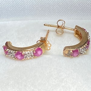 May include: A pair of gold hoop earrings with pink and white gemstones. The earrings have a curved shape and are set with small, round stones.