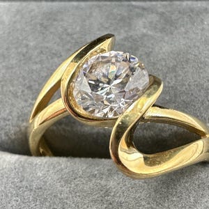 May include: A gold ring with a large, clear, round gemstone set in a unique, curved design.