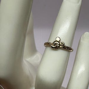 May include: A gold ring with a Mickey Mouse head design. The ring is on a mannequin finger.
