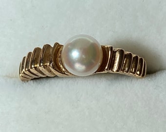 May include: A gold ring with a single white pearl set in the center. The band of the ring is textured with a wavy design.