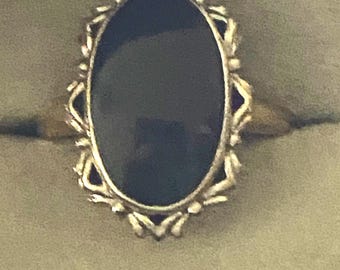 May include: A gold ring with a black oval gemstone set in a delicate, ornate design.