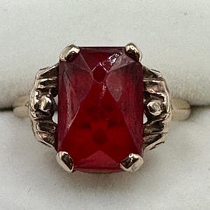 May include: A silver ring with a large, red, faceted gemstone. The ring has a detailed, ornate design.