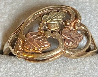 May include: A gold ring with a heart-shaped design featuring three leaves in a black and gold colour scheme.