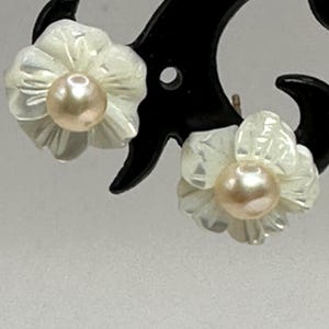 May include: A pair of white flower-shaped earrings with a pearl in the center of each flower.