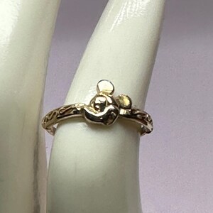 May include: A gold ring with a Mickey Mouse head design. The ring has a delicate, engraved band.