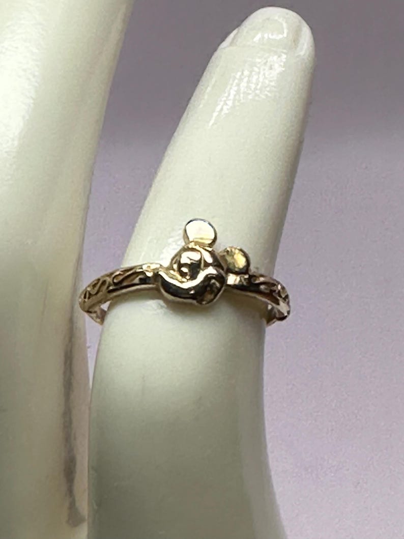 May include: A gold ring with a Mickey Mouse head design. The ring has a delicate, engraved band.