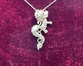 May include: A gold dragon pendant necklace with red gemstone eyes. The dragon is curled up with its tail in its mouth. The necklace is on a red velvet background.