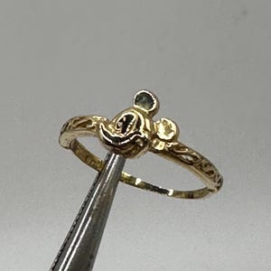 May include: A gold ring with a Mickey Mouse head design. The ring is thin and has a delicate design.