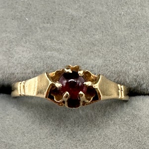 May include: A gold ring with a red gemstone set in a decorative, flower-like design.