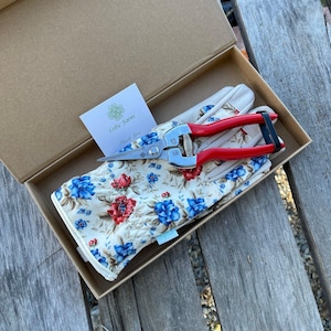 May include: A gardening gift set in a cardboard box. The set includes floral print gardening gloves, red-handled pruning shears, and a card that reads "Celtic Farm Thank You". The gloves have a cream background with blue and red flowers.