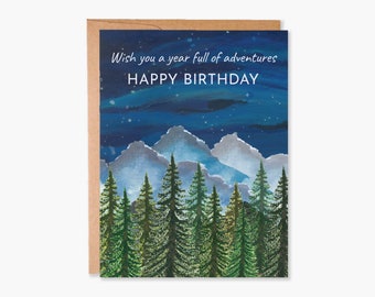May include: A birthday card with a watercolor illustration of a forest scene with mountains in the background. The card has the text "Wish you a year full of adventures" and "HAPPY BIRTHDAY" on it.