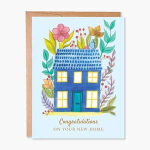 May include: A greeting card with a blue house illustration surrounded by flowers and foliage. The house has a blue roof and yellow windows. The text "Congratulations ON YOUR NEW HOME" is at the bottom of the card. The card is inside a brown envelope.