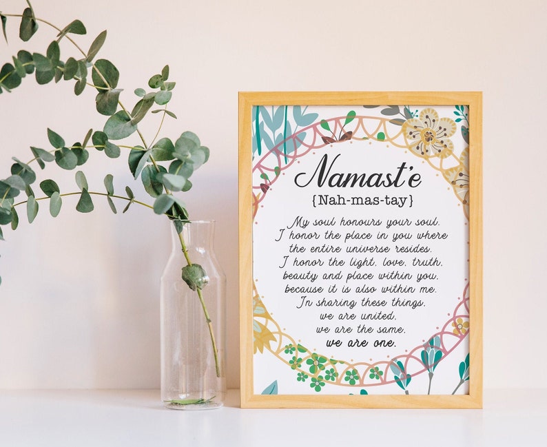 May include: A framed print with a floral design and the word "Namaste" in a decorative font. The text below defines the word as "Nah-mas-tay" and includes a short poem about the meaning of the word.