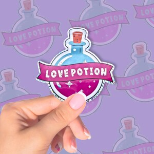 Puede incluir: Una pegatina que representa una botella de poción azul con líquido rosa y un corcho. La botella lleva la etiqueta "LOVE POTION" en una pancarta rosa. La pegatina se sostiene sobre un fondo de diseños repetidos de botellas de poción.
