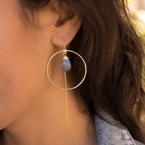 May include: Gold hoop earrings with a dangling teardrop-shaped blue gemstone.