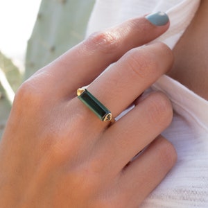 May include: A gold ring featuring a dark green rectangular gemstone. The ring has a pointed design on each side of the gemstone.