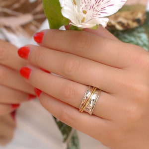 Op de afbeelding: Een draaibare ring van zilver, goud en roségoud met een gehamerde textuur. De ring wordt gedragen aan een vinger.
