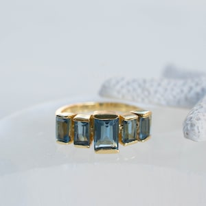 May include: A gold ring with five blue rectangular gemstones set in a row.