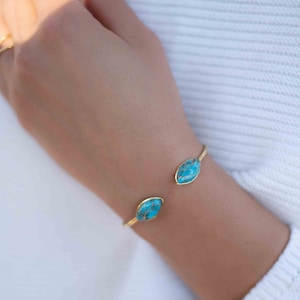 May include: A gold bangle bracelet with two turquoise oval-shaped stones.