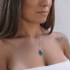 May include: A silver chain necklace with a teardrop-shaped pendant made of green gemstone.