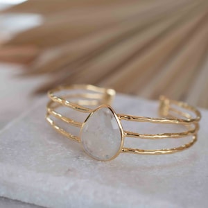 Puede incluir: Un brazalete de oro con una piedra preciosa transparente en forma de lágrima en el centro. El brazalete tiene tres bandas de oro.