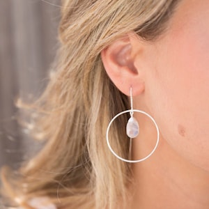 May include: Silver hoop earrings with a dangling pear-shaped gemstone.