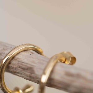 May include: A pair of gold hoop earrings with a simple, minimalist design. The earrings are made of a smooth, polished metal and have a slightly curved shape.