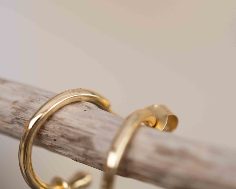 May include: A pair of gold hoop earrings with a simple, minimalist design. The earrings are made of a smooth, polished metal and have a slightly curved shape.