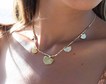May include: A gold necklace with a delicate chain and multiple small, circular pendants. The pendants have a textured, concentric circle design. The necklace is worn by a person with brown hair.