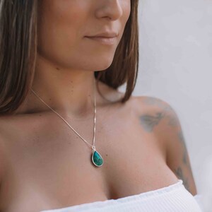 May include: A silver chain necklace with a teardrop-shaped pendant made of a dark green gemstone.