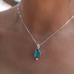 May include: A silver chain necklace with a teardrop-shaped pendant featuring a blue gemstone.