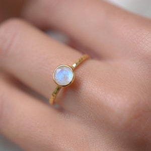May include: A gold ring with a round, white moonstone. The ring has a hammered texture.