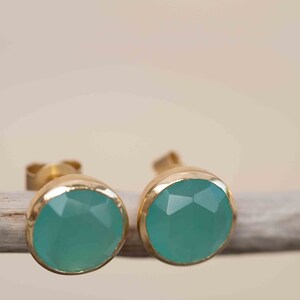May include: A pair of gold stud earrings with teal gemstone accents.