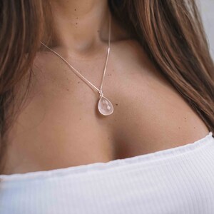 May include: A silver chain necklace with a teardrop-shaped rose quartz pendant.