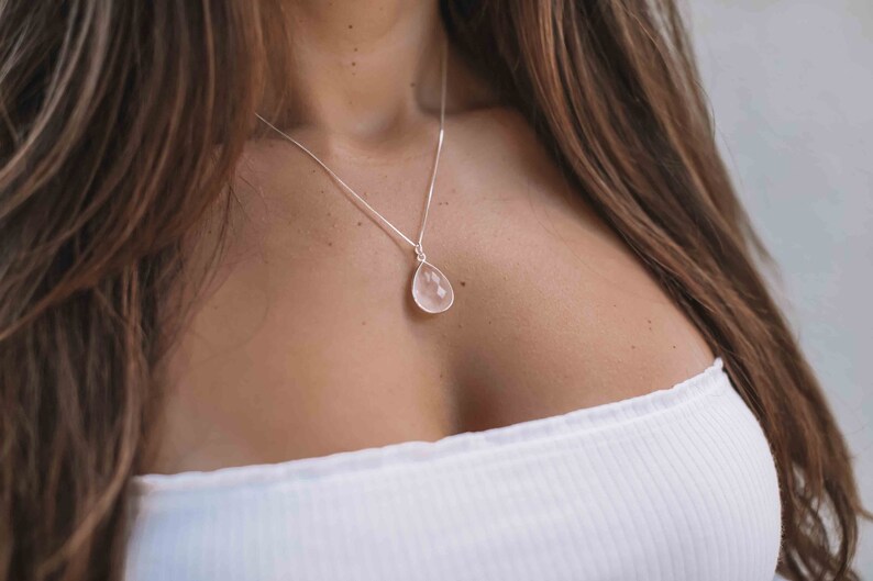 May include: A silver chain necklace with a teardrop-shaped rose quartz pendant.