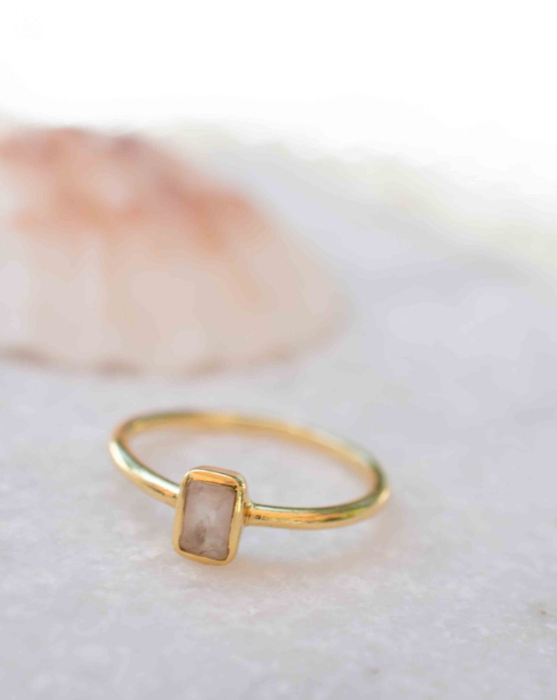 May include: A gold ring with a rectangular, light pink stone set in the center.