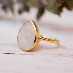 May include: A gold ring with a pear-shaped moonstone gemstone. The ring is set in a simple band.