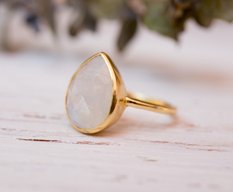 May include: A gold ring with a pear-shaped moonstone gemstone. The ring is set in a simple band.