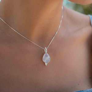 May include: A silver chain necklace with a teardrop-shaped moonstone pendant. The pendant has a delicate silver design around the edges.
