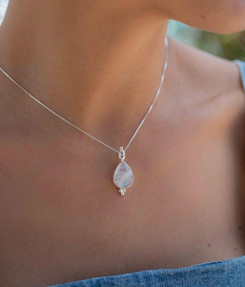 May include: A silver chain necklace with a teardrop-shaped moonstone pendant. The pendant has a delicate silver design around the edges.