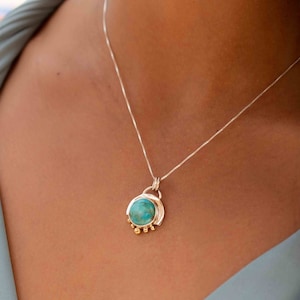 May include: A silver chain necklace with a turquoise stone pendant. The pendant is set in a silver frame with gold accents.