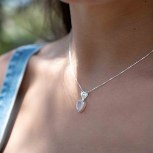 May include: A silver chain necklace with a rose quartz pendant. The pendant is a light pink color and has a teardrop shape.