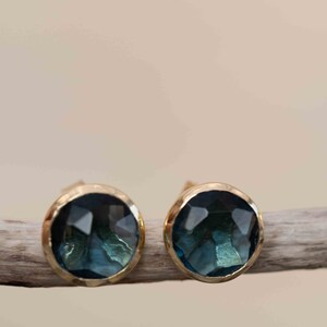 May include: A pair of gold stud earrings with a dark blue gemstone in each. The gemstones are faceted and have a slightly textured surface.