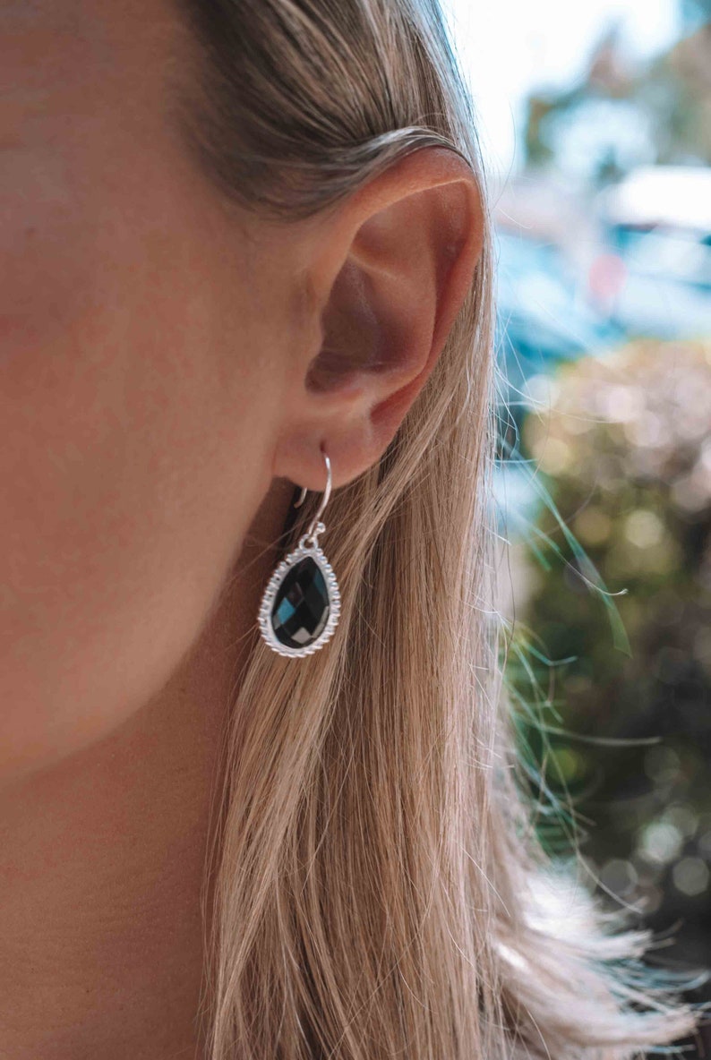 May include: A pair of silver dangle earrings with a black teardrop-shaped gemstone. The earrings have a delicate, intricate design.