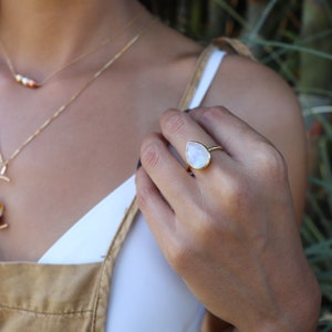 May include: A gold ring with a teardrop-shaped moonstone. The ring is on a person's finger.