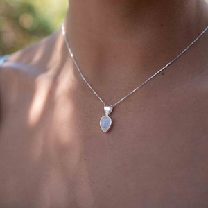 May include: A silver chain necklace with a teardrop-shaped moonstone pendant.