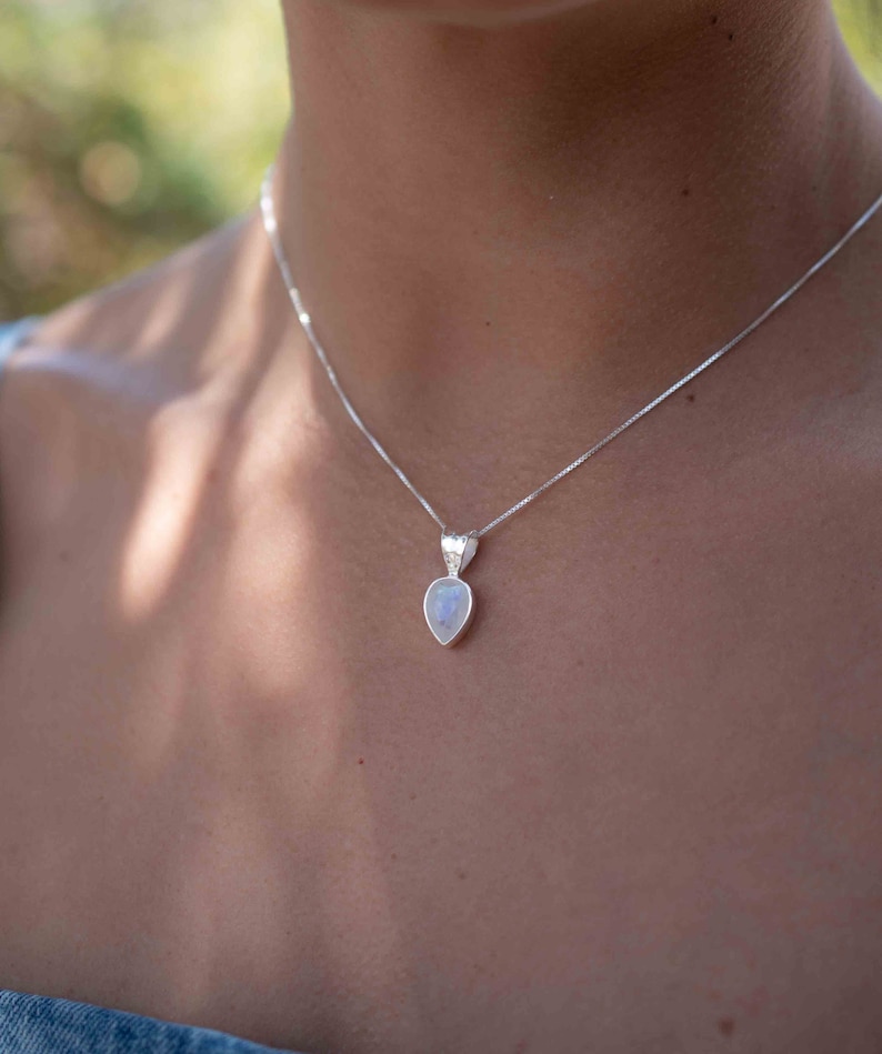 May include: A silver chain necklace with a teardrop-shaped moonstone pendant.