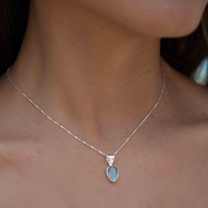 May include: A silver chain necklace with a teardrop-shaped pendant featuring a blue-green gemstone.